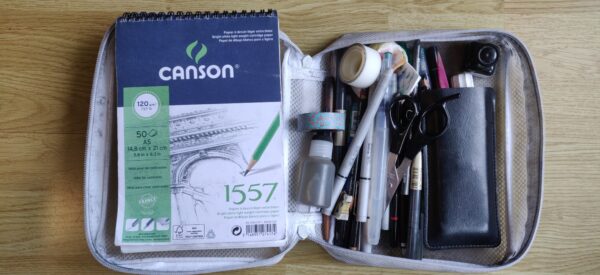 Un carnet et du matériel de dessin dans une grosse trousse