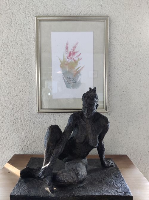 Un tableau avec une forme colorée pouvant évoquer le végétal et du texte, devant une scupture de femme assise