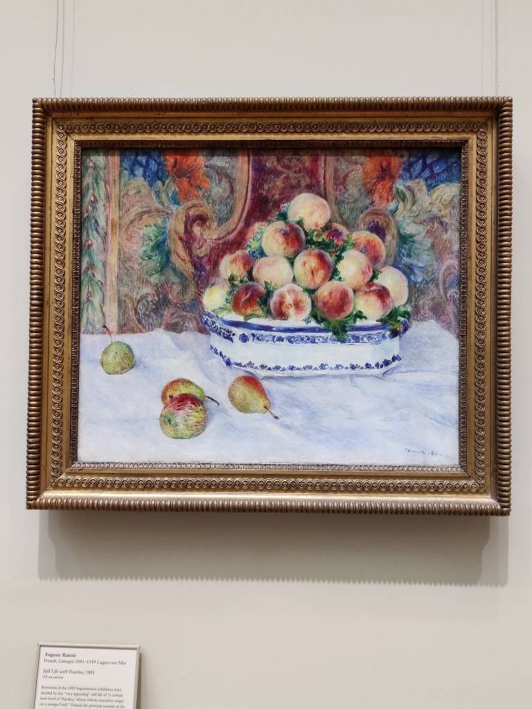 Amoncellement de pêches dans un saladier blanc à décor bleu avec quelques fruits posés devant sur une nappe blanche