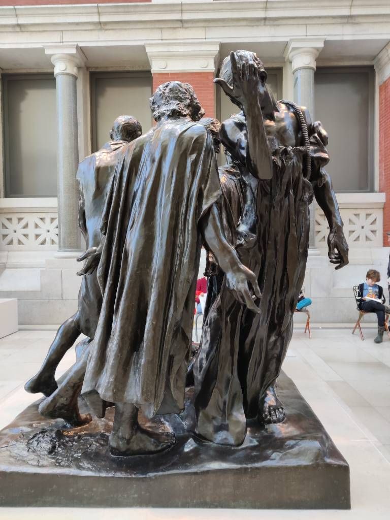 Sculpture en bronze grandeur nature. Depuis l'angle de vue choisi, on voit deux hommes debout en guenilles, l'un de dos la tête penchée, bras écartés, l'autre un bras levé vers le ciel lui cachant le visage. Derrière, on aperçoit d'autres personnages.