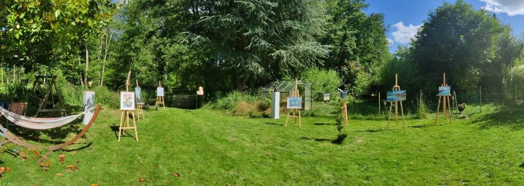 Panorama d'un jardin arboré où l'on aperçoit un hamac, une balancelle, des tableaux sur chevalets et des sculptures sur socles