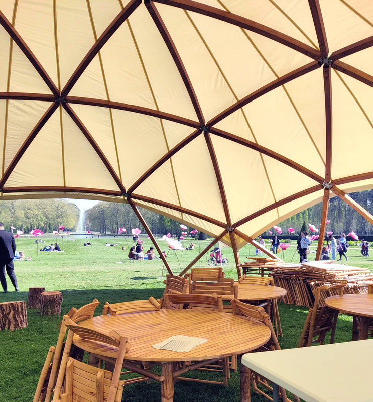 Une structure en toile et bois dans un parc, et des tables en dessous