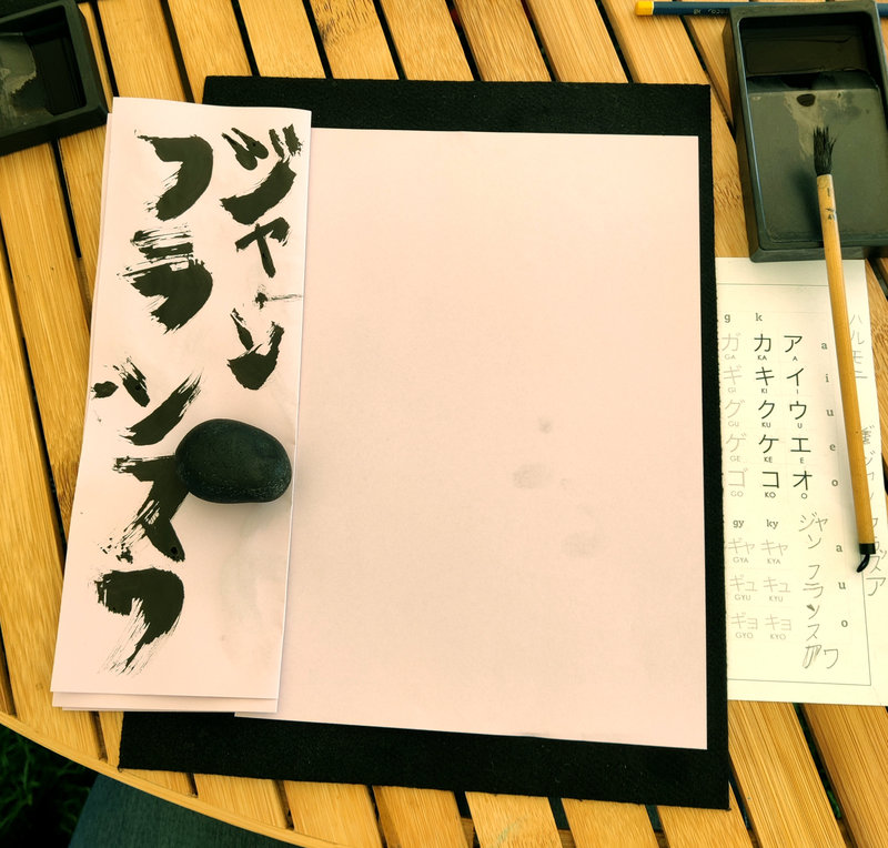 Matériel à calligraphie japonaise : une feuille d'essai, une feuille vierge, une feutrine sur le fond, un pinceau, une "pierre à frotter", une feuille avec les modèles